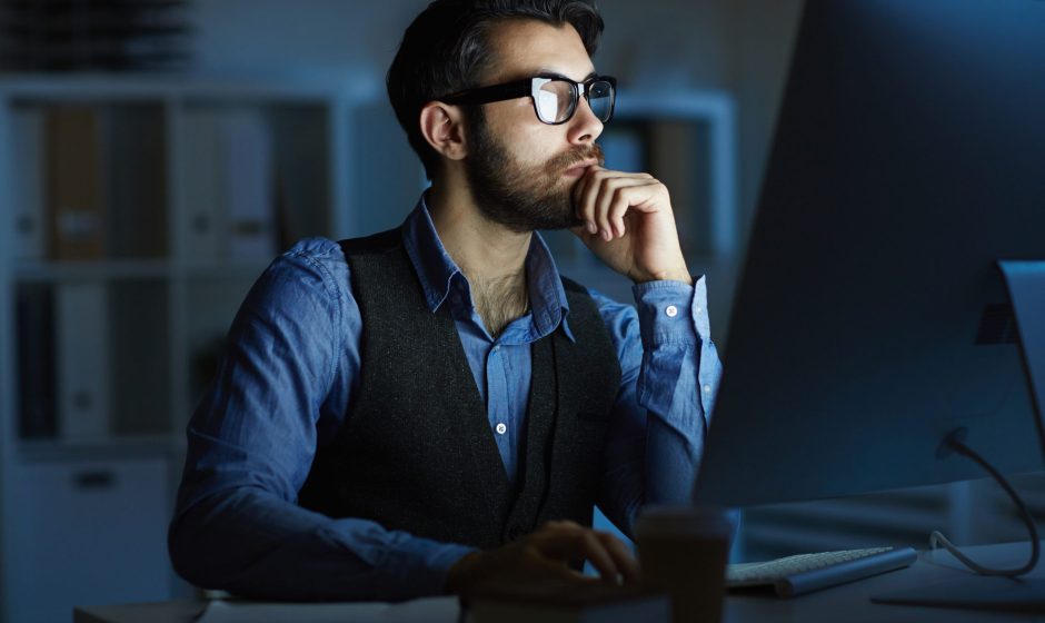 Concentrated entrepreneur or manager sitting by desk in front of computer monitor while working at night
